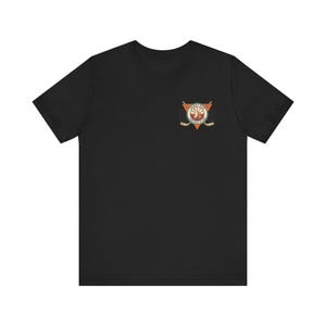 May include: Black t-shirt featuring a small, colorful emblem on the chest. The emblem includes a circle with text, a sun, and crossed hockey sticks, set within a triangle. The shirt is made of a soft material.