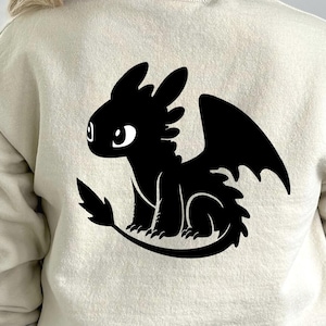Könnte beinhalten: Beiges Sweatshirt mit schwarzer Drachensilhouette. Der Drache hat große Flügel, einen langen Schwanz und große Augen. Das Design ist auf der Rückseite des Sweatshirts zentriert.