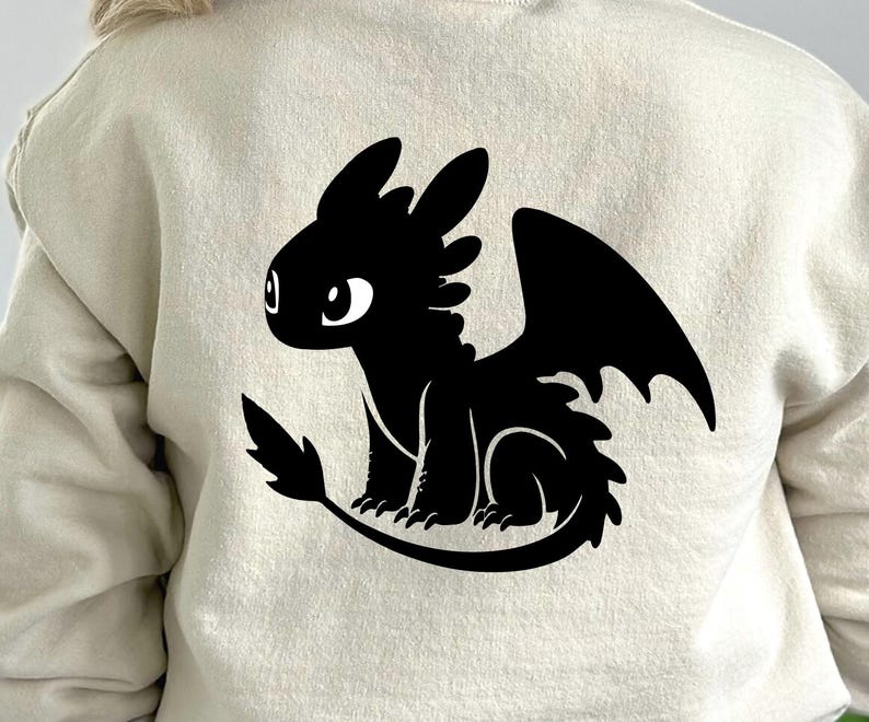 May include: A beige sweatshirt featuring a black silhouette of a dragon. The dragon has large wings, a long tail, and big eyes. The design is centered on the back of the sweatshirt.