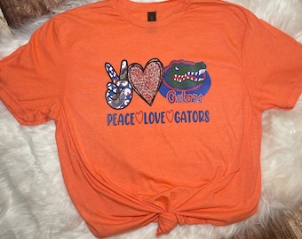 May include: Orange t-shirt with a peace sign, heart, and alligator graphic. The text "Peace Love Gators" is printed below the graphic.