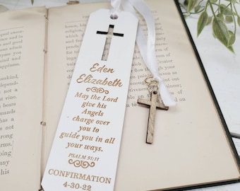 May include: White wooden bookmark with a gold cross and the text "Eden Elizabeth" and "May the Lord give his Angels charge over you to guide you in all your ways. Psalm 91:11 Confirmation 4-30-22".