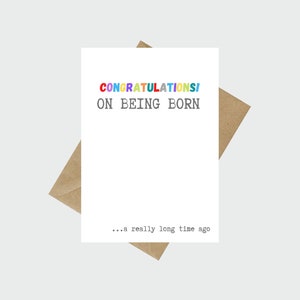 May include: A white card with the text "CONGRATULATIONS! ON BEING BORN... a really long time ago" in black and colorful letters.