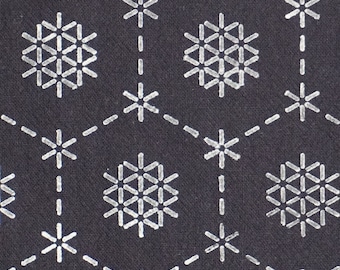 May include: A dark gray fabric with a repeating pattern of white snowflake-like designs. The snowflakes are made up of small lines that form a geometric shape.