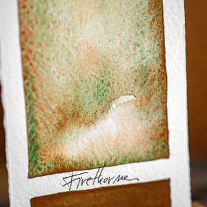 Peut inclure: Un échantillon de peinture aquarelle avec un dégradé de couleur vert et marron. L'échantillon est étiqueté "Firethorne".