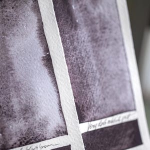 以下が含まれることがあります： テクスチャード加工された紙に水彩絵の具の見本が描かれています。見本は茶色とグレーの色合いで、白いハイライトがあります。紙は白い線で区切られ、手書きの文字が見えます。