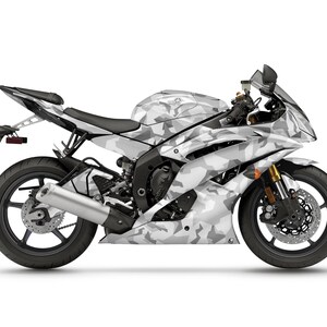 Pu&ograve; includere: Una motocicletta Yamaha con mimetica bianca e grigia. La moto sportiva ha ruote nere, un sedile nero e forcelle anteriori dorate. La motocicletta &egrave; su sfondo bianco.