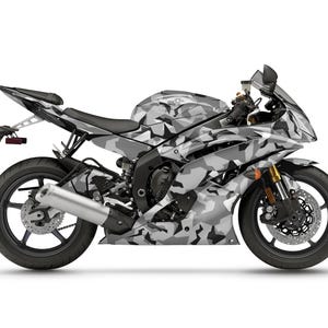 Pu&ograve; includere: Una moto sportiva con un motivo mimetico grigio e bianco. La moto ha ruote nere, un sedile nero e forcelle anteriori dorate. Il design copre la carenatura, il serbatoio del carburante e altre parti della carrozzeria.