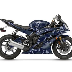 Pu&ograve; includere: Una moto sportiva Yamaha R6 con un motivo mimetico blu e bianco. La moto ha ruote nere, uno scarico argentato e forcelle anteriori dorate. Lo sfondo &egrave; bianco.