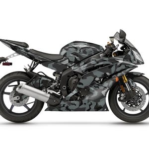 Pu&ograve; includere: Una motocicletta Yamaha R6 con mimetica nera e grigia. La moto sportiva ha una sella nera, scarico argentato e forcelle anteriori dorate. La moto &egrave; su sfondo bianco.