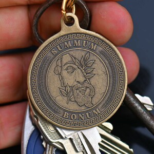 May include: A bronze key chain with a round medallion featuring a profile of a man with a laurel wreath and the text "SUMMUM BONUM" in a Greek key border.