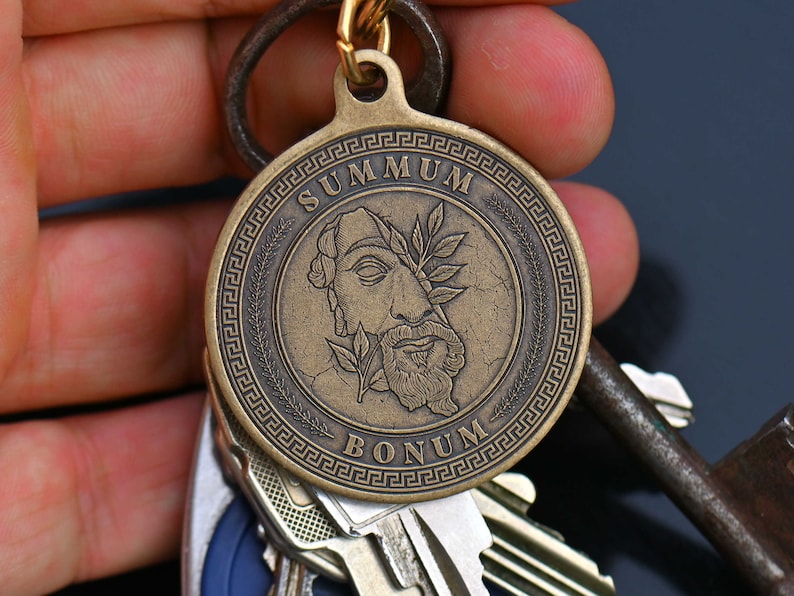 May include: A bronze key chain with a round medallion featuring a profile of a man with a laurel wreath and the text "SUMMUM BONUM" in a Greek key border.