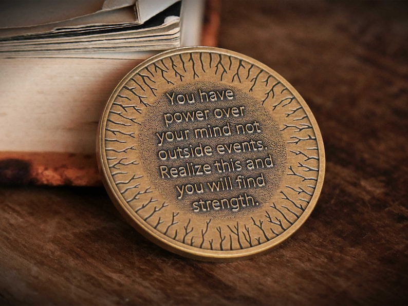 May include: A round, bronze-colored coin with a tree-like design and the inscription "You have power over your mind not outside events. Realize this and you will find strength."