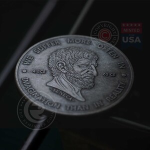 May include: A silver coin with a profile of Seneca the Younger, a Roman philosopher, on one side. The coin reads "We suffer more often in imagination than in reality."  The other side of the coin reads "4 BCE - Seneca - 65 CE" and has a copyright symbol.