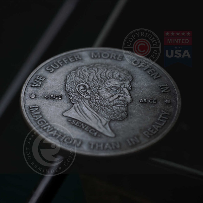 May include: A silver coin with a profile of Seneca the Younger, a Roman philosopher, on one side. The coin reads "We suffer more often in imagination than in reality."  The other side of the coin reads "4 BCE - Seneca - 65 CE" and has a copyright symbol.
