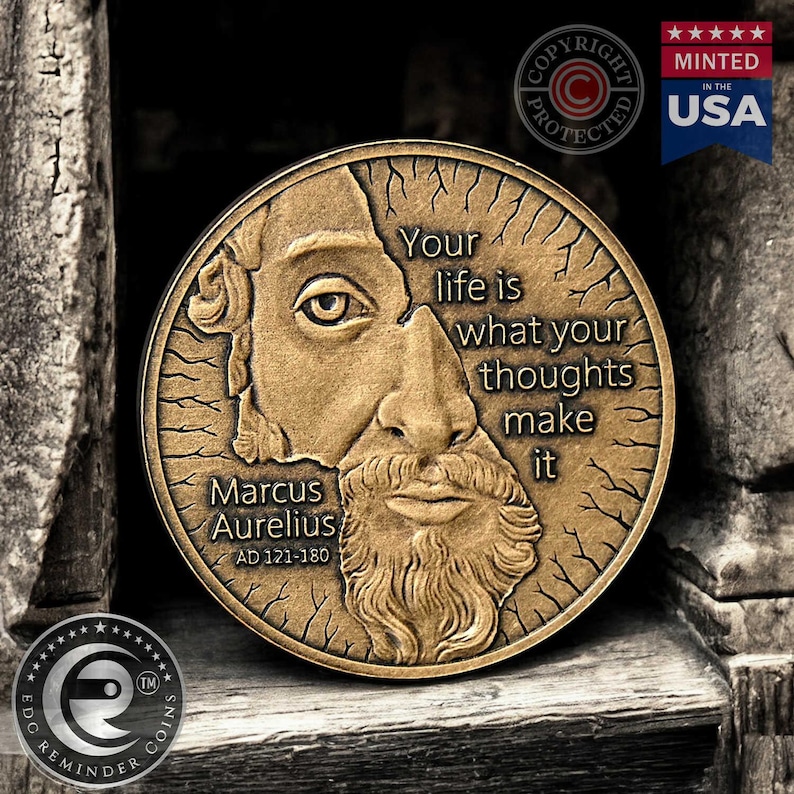 May include: A bronze coin with a portrait of Marcus Aurelius and the quote "Your life is what your thoughts make it". The coin is surrounded by a decorative border and has the words "Marcus Aurelius AD 121-180" inscribed on it.