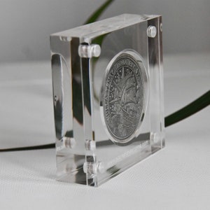May include: A silver coin with the inscription "TENEAC INVIA EST VIA" is displayed in a clear acrylic coin holder. The coin features a ship with sails and a compass.