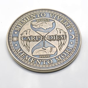 May include: A silver-toned coin with a blue background and gold lettering. The coin features an hourglass with wings and the text "Memento Vivere", "Tempus Fugit", "Carpe Diem", and "Memento Mori".