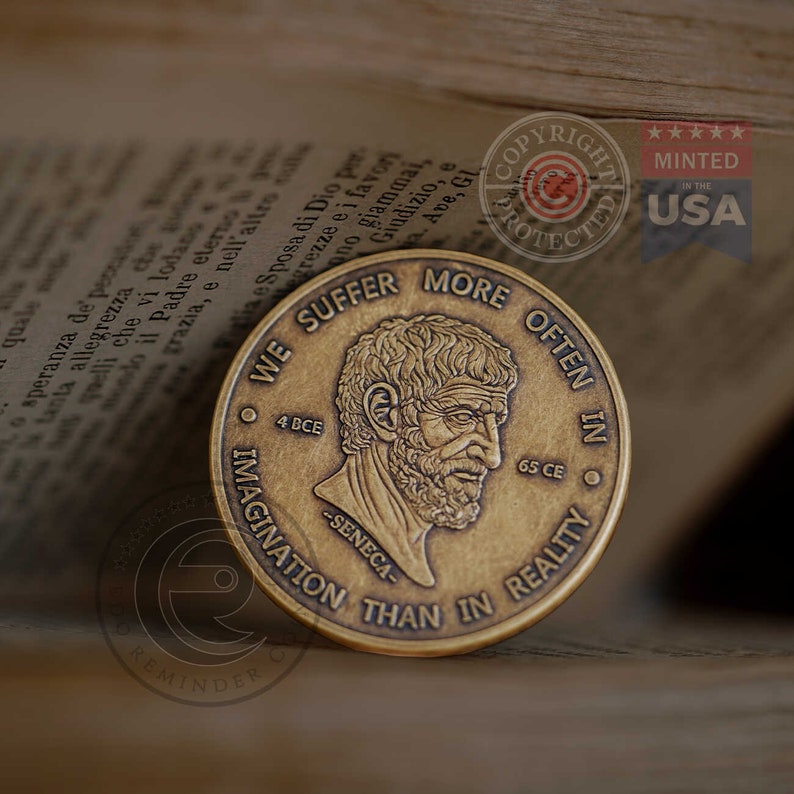 May include: A round, antique-finish brass coin featuring a relief portrait of Seneca in the center. The text reads WE SUFFER MORE OFTEN IN IMAGINATION THAN IN REALITY, with 4 BCE and 65 CE flanking the portrait and the name SENECA below it.
