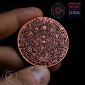 May include: A copper-colored coin with a circular design featuring an atom symbol, a sun, and a moon. The coin has the text "As Above, So Below As Within, So Without As The Universe, So The Soul" around the edge.