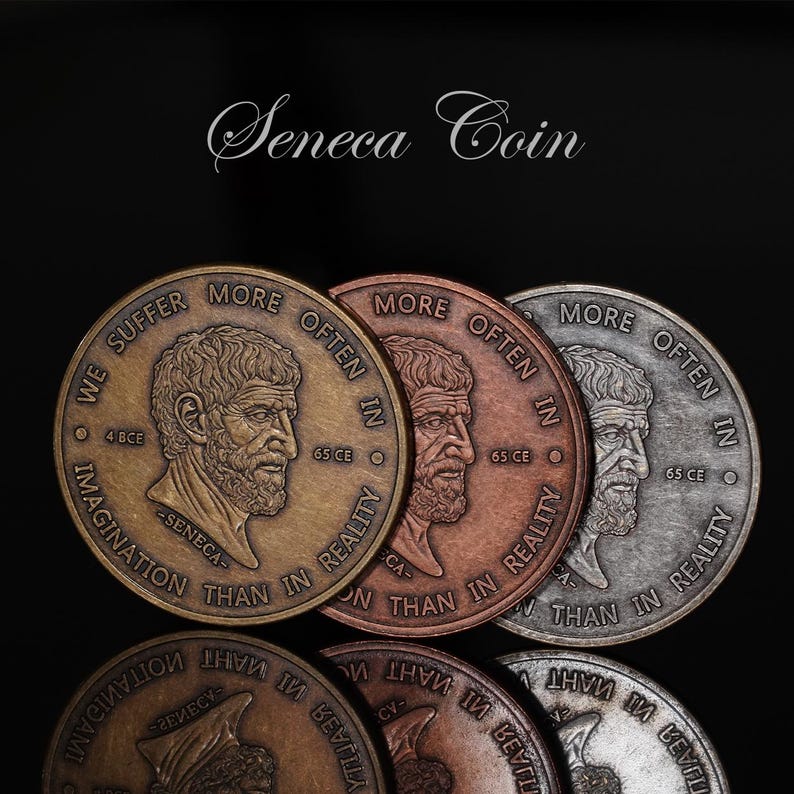 May include: Three circular metal coins in bronze, copper, and silver tones featuring a profile portrait of Seneca. The text reads WE SUFFER MORE OFTEN IN IMAGINATION THAN IN REALITY, 4 BCE, 65 CE, and SENECA. The words Seneca Coin appear above.