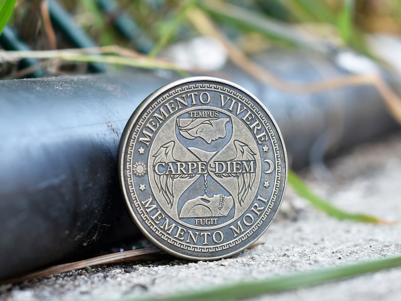 May include: A round, bronze-colored coin with an hourglass design and the Latin phrases "Memento Vivere", "Carpe Diem", and "Memento Mori".