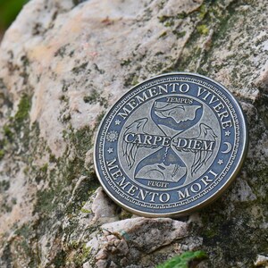 May include: A silver-toned round coin with an hourglass design and the Latin phrases "Memento Vivere", "Carpe Diem", and "Memento Mori" inscribed around the edge.