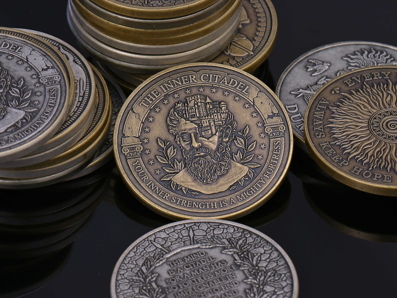 Op de afbeelding: Een verzameling ronde metalen munten met een antieke afwerking. De centrale munt toont een reli&euml;f van een bebaard hoofd met een kasteel erbovenop, met de inscripties THE INNER CITADEL en YOUR INNER STRENGTH IS A MIGHTY FORTRESS.