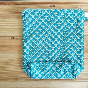 May include: A rectangular zippered pouch, 25cm x 29cm, with a teal and gold geometric pattern. The pouch has a small fabric loop on the side. The background is a light brown wooden surface.