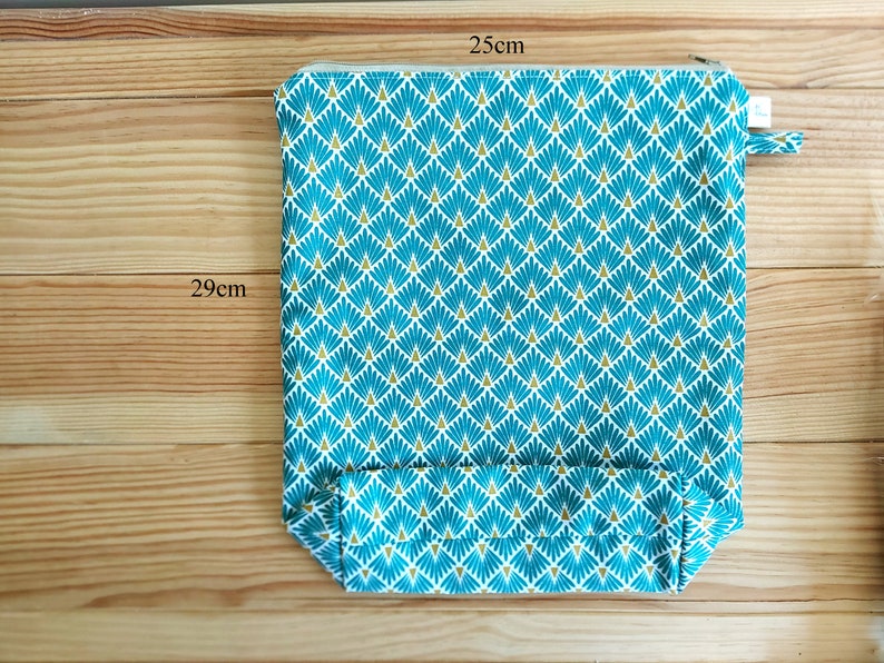 May include: A rectangular zippered pouch, 25cm x 29cm, with a teal and gold geometric pattern. The pouch has a small fabric loop on the side. The background is a light brown wooden surface.
