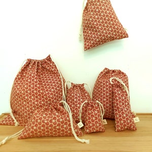 May include: Set of six red and white drawstring bags with a geometric pattern. The bags are made of fabric and come in various sizes.