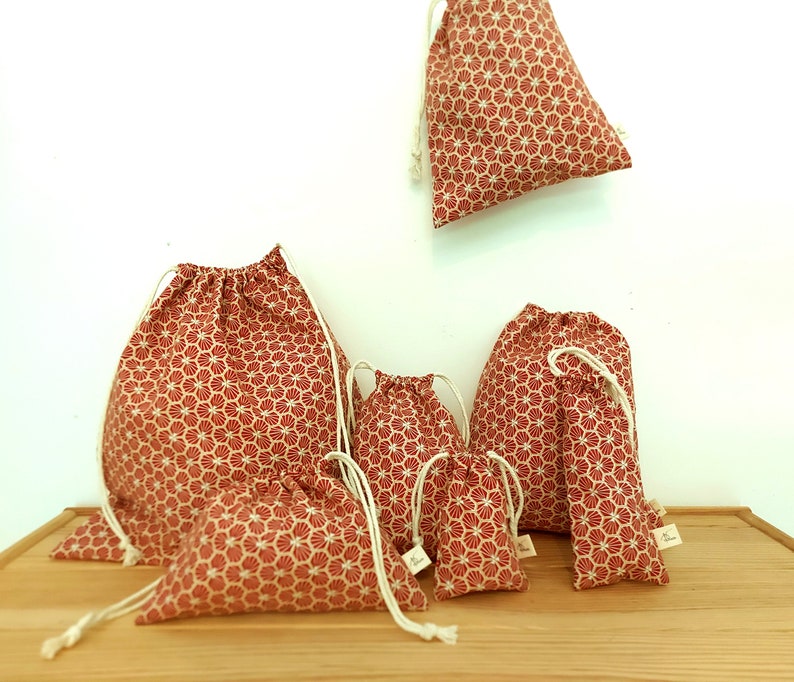May include: Set of six red and white drawstring bags with a geometric pattern. The bags are made of fabric and come in various sizes.