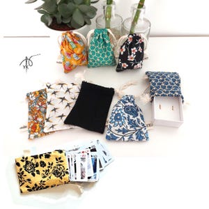 Può includere: Una collezione di piccole borse con coulisse in vari modelli, tra cui motivi floreali, geometrici e di uccelli. Alcune borse sono aperte, rivelando piccoli oggetti, mentre altre sono chiuse con un cordoncino. Sono visibili anche carte da gioco.