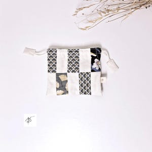 Op de afbeelding: Een kleine patchwork-pouch met een trekkoordsluiting. De pouch heeft een mix van witte, zwarte en bedrukte stoffen vierkanten. Sommige vierkanten hebben een waaierachtig ontwerp, andere een bloemenpatroon en weer andere een ginkgo-bladontwerp.