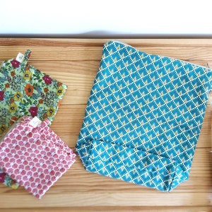 May include: Three fabric pouches with zipper closures rest on a wooden surface. One is teal with a geometric pattern, another is green with a floral print, and the third is pink with a honeycomb design. The pouches vary in size.