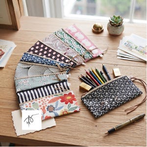 Peut inclure: Une collection de trousses à crayons rectangulaires en tissu présentant divers motifs, notamment floraux, rayés et géométriques. Une trousse est ouverte, remplie de crayons de couleur et d'une gomme dorée, tandis que les autres sont en éventail.