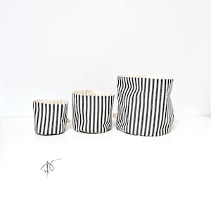 May include: Three fabric storage containers in varying sizes. Each container features a black and white striped pattern on the exterior and a cream-colored interior. The containers are cylindrical and appear to be made of a soft, pliable material.