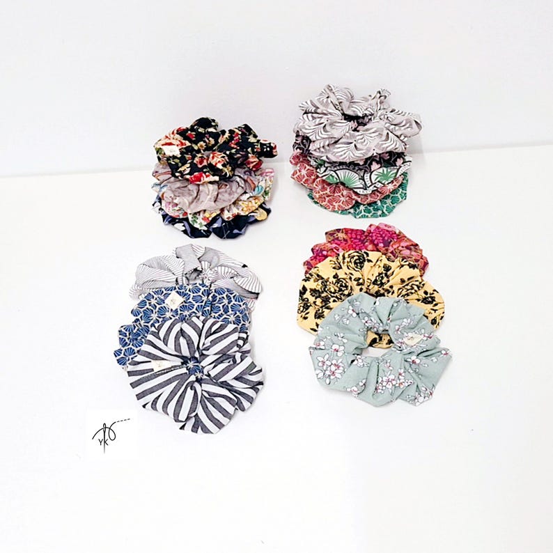 Pu&ograve; includere: Una collezione di elastici per capelli in tessuto colorato con vari disegni floreali e fantasia. Gli elastici sono impilati in piccoli mucchi, mostrando una variet&agrave; di colori tra cui nero, rosso, giallo, blu e verde. Gli elastici sono in tessuto morbido.