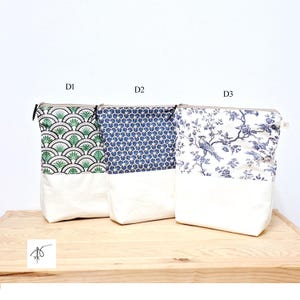 May include: Three zippered pouches with different patterned tops and white bottoms are displayed on a wooden surface. The patterns include green and white fan shapes, blue geometric designs, and a blue bird and floral print. The pouches are labeled D1, D2, and D3.