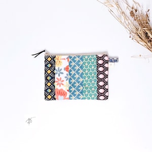 May include: A rectangular patchwork zip pouch with a black zip pull. The pouch features fabric panels with diverse patterns, including geometric shapes, floral designs, and a teal scallop pattern. The pouch is on a white background.
