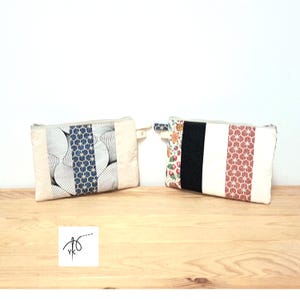 Peut inclure: Deux pochettes rectangulaires en tissu avec fermeture éclair. La pochette de gauche présente un motif géométrique bleu et blanc central entouré de motifs en éventail et de panneaux crème. Celle de droite arbore un imprimé fraise, une bande noire.