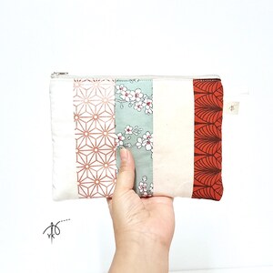 Peut inclure: Une pochette rectangulaire à fermeture éclair composée de cinq bandes de tissu verticales. Le motif comprend une section blanche, un imprimé géométrique cuivré, un tissu floral vert clair, une bande crème et un motif en éventail rouge foncé.