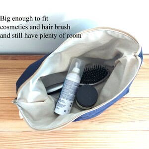 May include: A navy blue cosmetic bag with a beige interior, open to reveal a hairbrush, cosmetics, and other items. The bag has a zipper closure and the text "Big enough to fit cosmetics and hair brush and still have plenty of room".