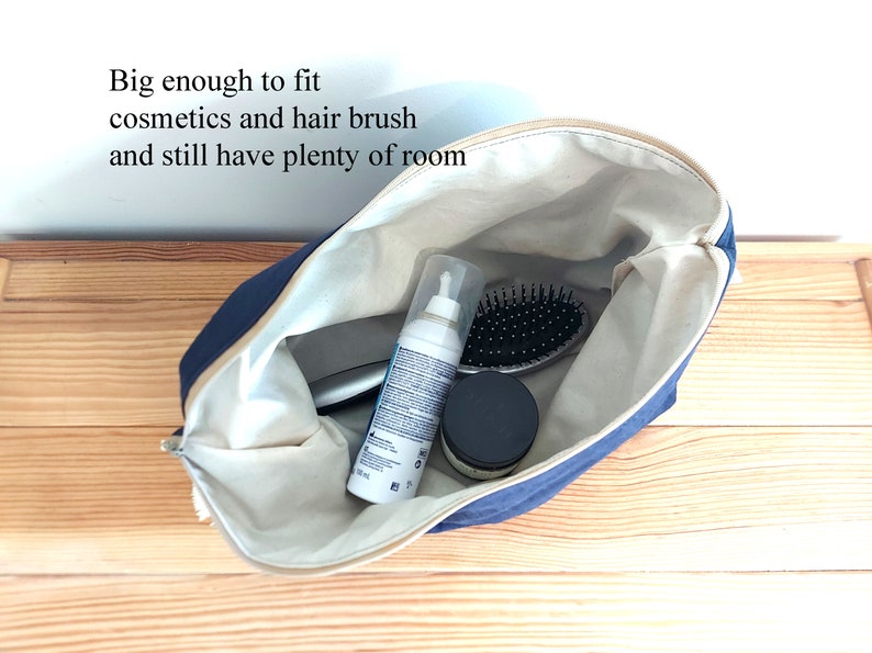 May include: A navy blue cosmetic bag with a beige interior, open to reveal a hairbrush, cosmetics, and other items. The bag has a zipper closure and the text "Big enough to fit cosmetics and hair brush and still have plenty of room".