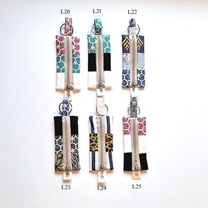 May include: Six rectangular fabric zipper pouches with key rings. Each pouch features a unique pattern, including floral, geometric, and animal prints, with a central white panel and a silver zipper. The pouches are labeled L20, L21, L22, L23, L24, and L25.