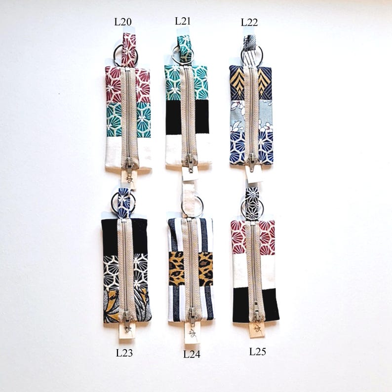 May include: Six rectangular fabric zipper pouches with key rings. Each pouch features a unique pattern, including floral, geometric, and animal prints, with a central white panel and a silver zipper. The pouches are labeled L20, L21, L22, L23, L24, and L25.