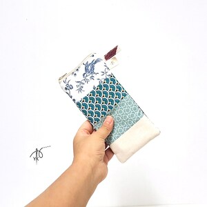 May include: A rectangular fabric pouch featuring a patchwork design with four distinct sections: a white panel with blue bird and floral motifs, a teal panel with gold fan patterns, a light blue geometric print, and a solid cream-colored base.