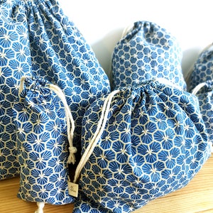 Pode incluir: Conjunto de cinco sacos de cord&atilde;o azul e dourado com um padr&atilde;o geom&eacute;trico. Os sacos s&atilde;o feitos de tecido e t&ecirc;m um cord&atilde;o branco.