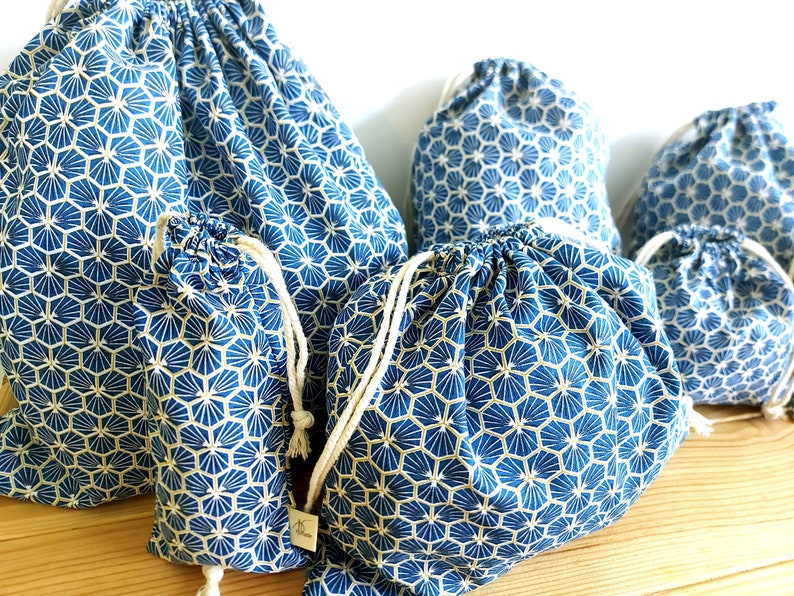 Pode incluir: Conjunto de cinco sacos de cord&atilde;o azul e dourado com um padr&atilde;o geom&eacute;trico. Os sacos s&atilde;o feitos de tecido e t&ecirc;m um cord&atilde;o branco.