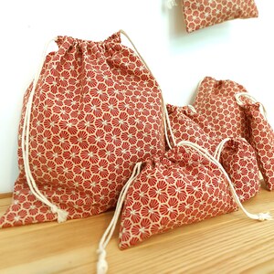 May include: Set of five red and white drawstring bags with a geometric pattern. The bags are made of fabric and have a white drawstring closure.