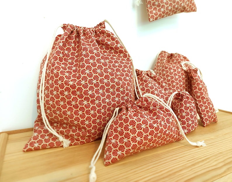 May include: Set of five red and white drawstring bags with a geometric pattern. The bags are made of fabric and have a white drawstring closure.
